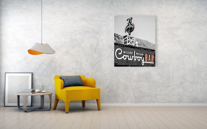 May include: Black and white photo of a sign for the "Million Dollar Cowboy Bar" in Wyoming. The sign features a cowboy riding a bucking bronco.