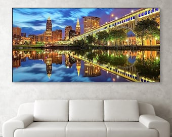 May include: A panoramic view of a city skyline at night, with tall buildings illuminated by lights, reflecting in the water. A bridge spans the river, with trees lining the banks. The sky is a deep blue with clouds.