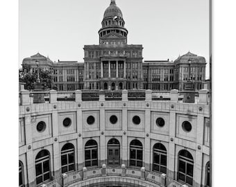 May include: A black and white photograph of the Texas State Capitol building in Austin, Texas. The building is seen from below, looking up at the dome. The building is surrounded by a circular structure with arches and windows.