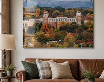 May include: A rectangular acrylic wall art print featuring a landscape view of a large brick building with two towers, surrounded by dense trees displaying autumn foliage in shades of orange, yellow, and red, mounted with four silver metal standoffs.