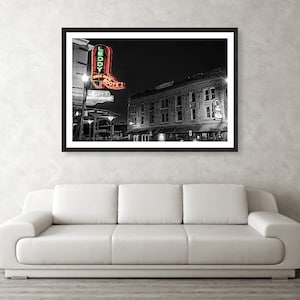 May include: Black and white photograph of a neon sign for "Leddy's Boots" in a city at night. The sign is shaped like a red cowboy boot with green neon lettering. The sign is in front of a brick building with windows.