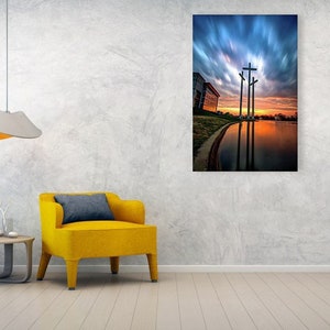 May include: Three large crosses silhouetted against a dramatic sunset sky with clouds. The crosses are reflected in a still body of water.