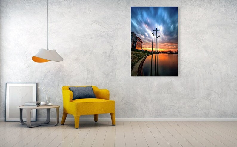 May include: Three large crosses silhouetted against a dramatic sunset sky with clouds. The crosses are reflected in a still body of water.