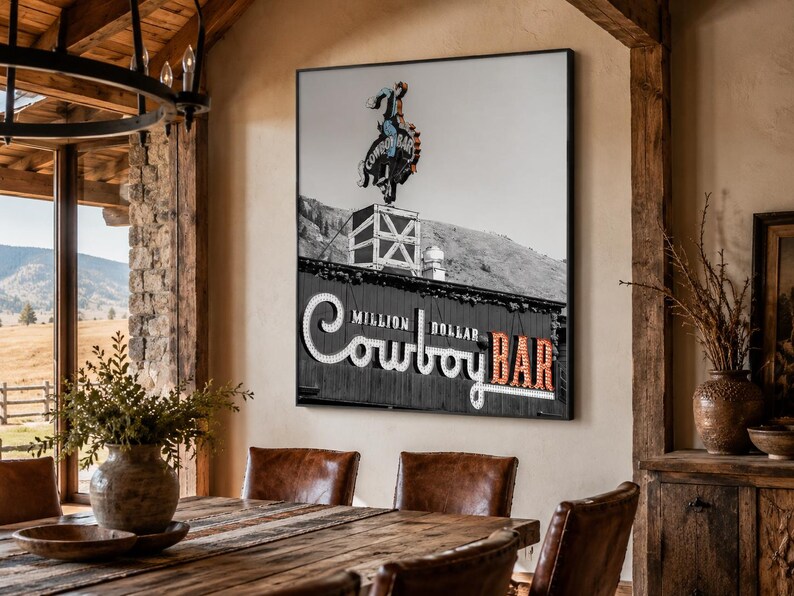 May include: A square wall art print featuring a black and white photograph of the Million Dollar Cowboy Bar sign. The image displays a neon cowboy figure atop a building, with the text Million Dollar Cowboy Bar in large, illuminated lettering.