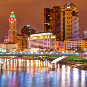 May include: A panoramic view of a city skyline at night. The city is lit up with lights, and there is a river flowing through the center of the image. There are several bridges crossing the river, and the buildings are all tall and modern.