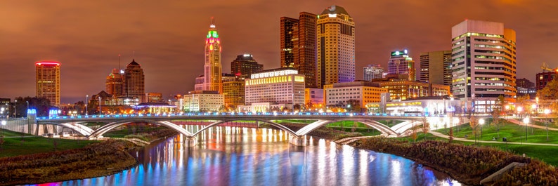 May include: A panoramic view of a city skyline at night. The city is lit up with lights, and there is a river flowing through the center of the image. There are several bridges crossing the river, and the buildings are all tall and modern.