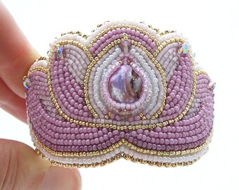 May include: A pink and white beaded flower brooch with a pearl-like center and gold accents.