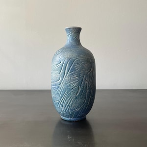 May include: A blue ceramic vase with a textured, swirling pattern. The vase has a narrow neck and a rounded body.