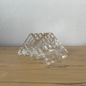 May include: A set of clear acrylic geometric coasters stacked in a triangular shape. The coasters are made of clear acrylic and have a smooth, polished finish.