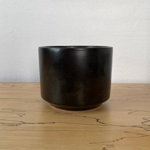 May include: A black ceramic planter with a smooth, glossy finish. The planter has a rounded base and straight sides.