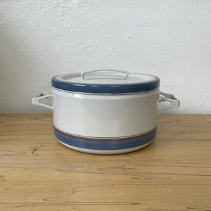 May include: A white ceramic pot with blue and brown stripes and a lid. The pot has two handles on the sides.