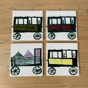 May include: Set of four ceramic tiles featuring black and white illustrations of a vintage train with different colored windows. The windows are green, red, yellow, and purple.