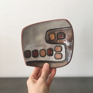 May include: A ceramic dish with a grey glaze and brown geometric designs. The dish has a unique shape and is perfect for serving snacks or appetizers.