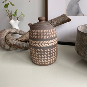 May include: A brown ceramic jar with a lid, featuring a geometric pattern of triangles and stripes in white and brown.