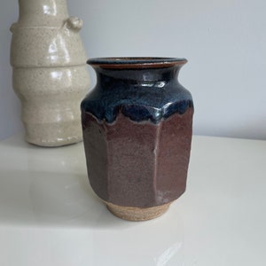 May include: A dark brown and blue ceramic vase with a geometric shape. The vase has a textured surface and a slightly uneven rim.