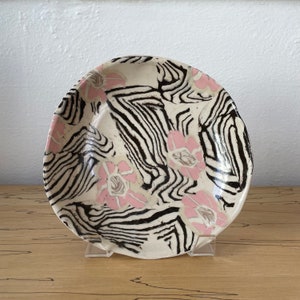 May include: A white ceramic plate with a black and white zebra stripe pattern and pink floral accents.
