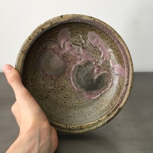 May include: A ceramic bowl with a speckled brown glaze and a pink and brown design. The bowl is handmade and has a rustic look.