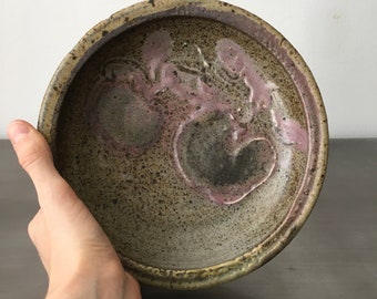 Könnte beinhalten: Eine Keramikschüssel mit einem gesprenkelten braunen Überzug und einem rosa-braunen Design. Die Schüssel ist handgefertigt und hat einen rustikalen Look.