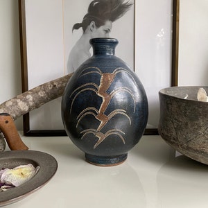 May include: A dark blue ceramic vase with a brown and white abstract design. The vase has a rounded body and a narrow neck.