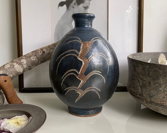 Könnte beinhalten: Eine dunkelblaue Keramikvase mit einem braunen und weißen abstrakten Design. Die Vase hat einen runden Körper und einen schmalen Hals.