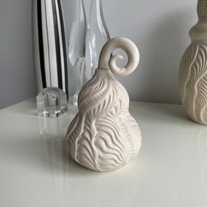 Peut inclure: Vase en céramique blanche avec un motif texturé en forme de feuille et un bec recourbé.