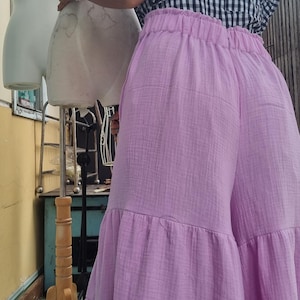May include: A person wearing a black and white checkered top with ruffled sleeves and light purple wide-leg pants. The pants have a tiered design. A mannequin is in the background.