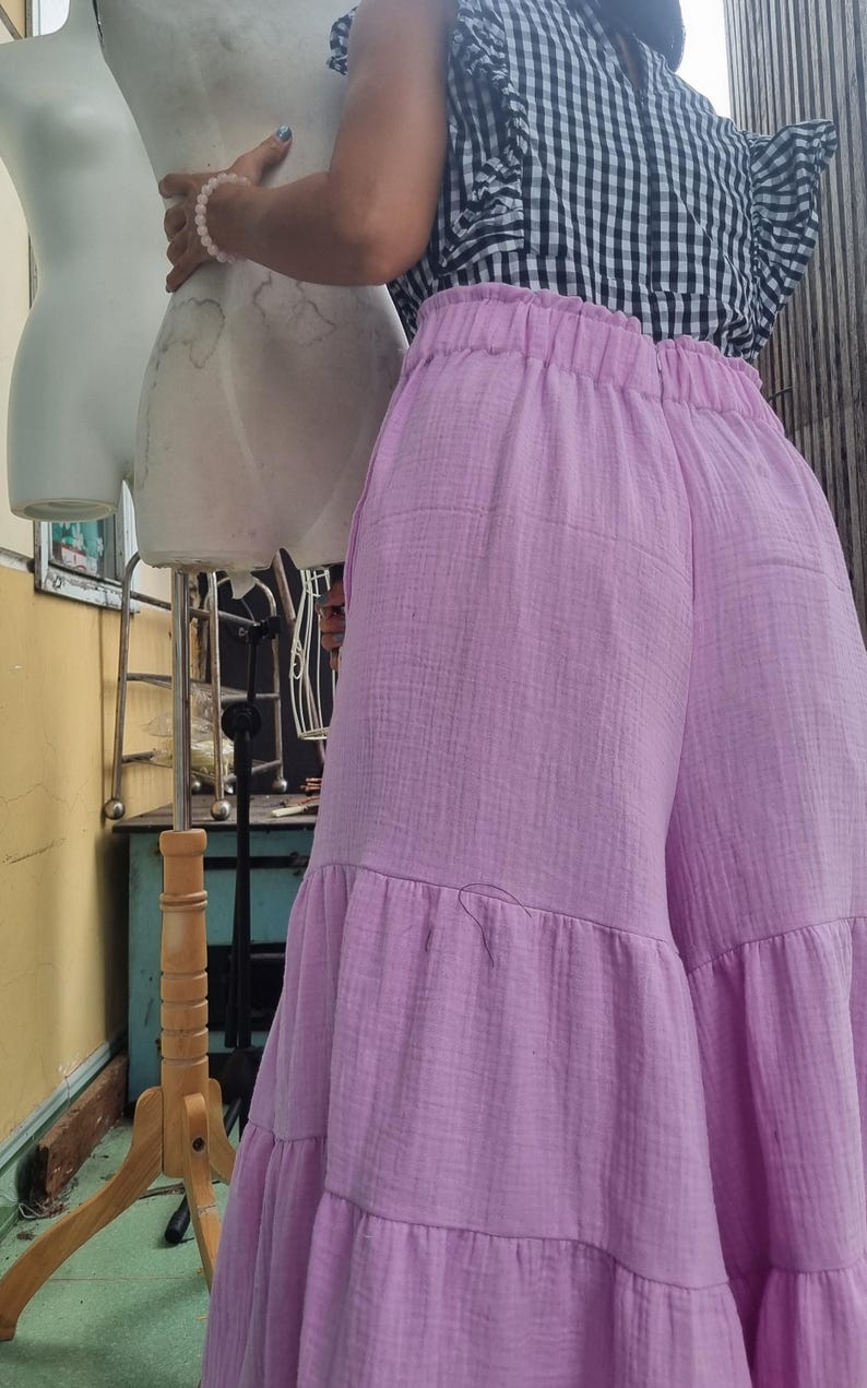 May include: A person wearing a black and white checkered top with ruffled sleeves and light purple wide-leg pants. The pants have a tiered design. A mannequin is in the background.