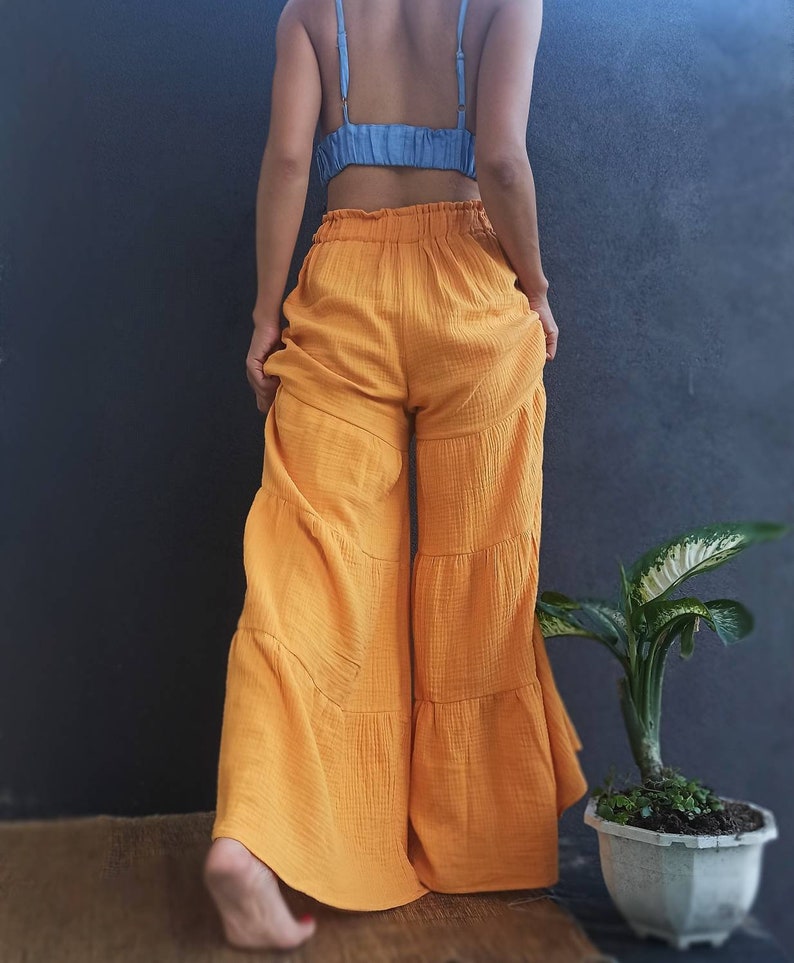 May include: Mustard yellow wide-leg pants with a tiered design. The pants have an elastic waistband and are paired with a light blue crop top. The outfit is casual and comfortable, suitable for warm weather.