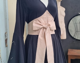 Könnte beinhalten: Schwarzes Kleid mit langen, ausgestellten Ärmeln und V-Ausschnitt. Das Kleid hat einen breiten, hellbraunen Schärpe, die in einer Schleife in der Taille gebunden ist. Das Kleid wird auf einer Schaufensterpuppe präsentiert.
