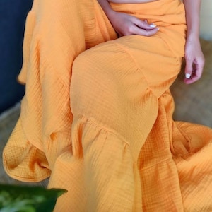 May include: A flowing, bright orange skirt with a ruffled hem. The fabric appears to be a lightweight, textured material. The skirt is draped, suggesting a comfortable fit. The overall style is casual and summery.