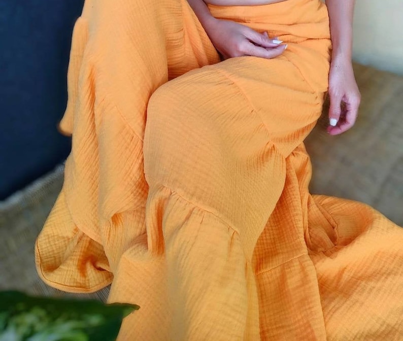 May include: A flowing, bright orange skirt with a ruffled hem. The fabric appears to be a lightweight, textured material. The skirt is draped, suggesting a comfortable fit. The overall style is casual and summery.