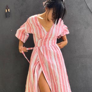 Peut inclure: Robe portefeuille à rayures roses et blanches, avec un col en V et des manches courtes. La robe a une taille nouée et une fente haute. Idéale pour l'été, elle est de longueur genou.