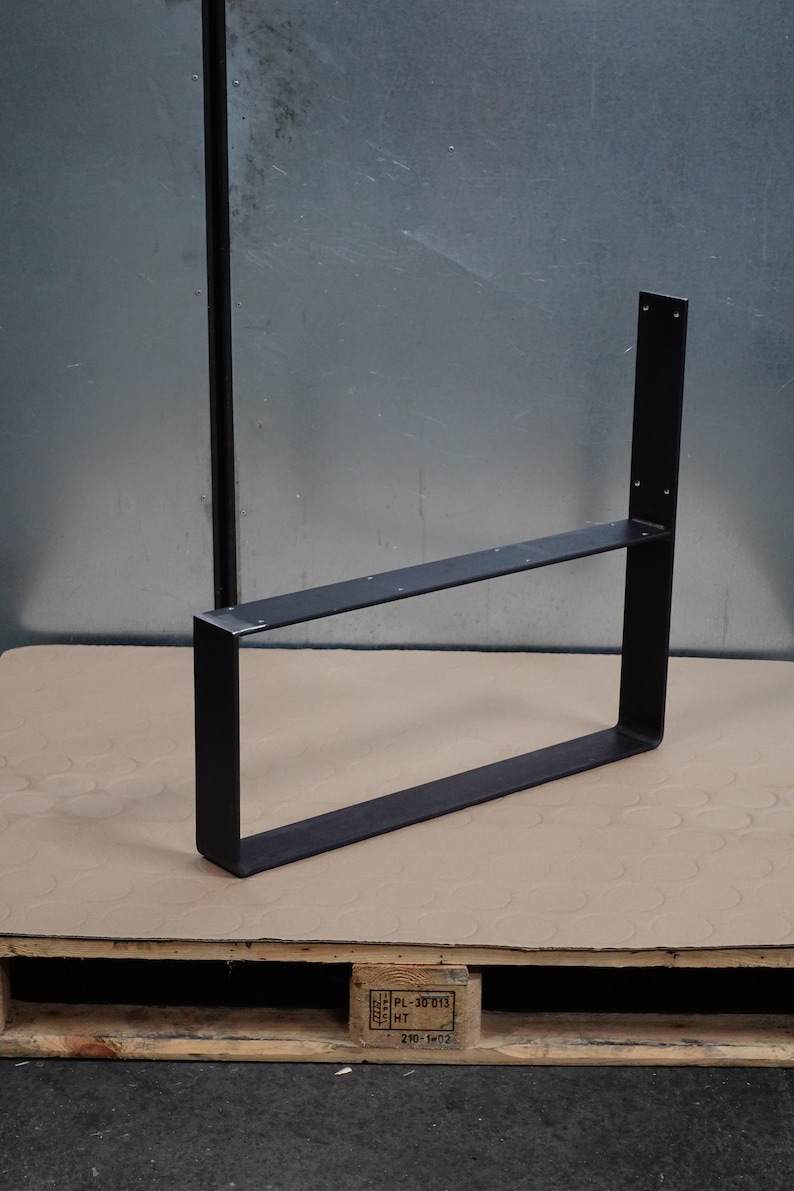 Pu&ograve; includere: Gambe da tavolo in metallo nero con forma rettangolare e un solo ripiano. La gamba &egrave; appoggiata su un pallet di legno.