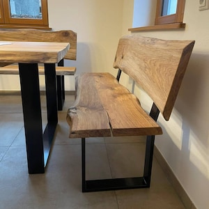 Könnte beinhalten: Holzbank mit Sitzfläche und Rückenlehne mit Baumkante, getragen von schwarzen Metallbeinen. Die natürliche Holzmaserung ist sichtbar, und die Bank ist Teil einer Essgruppe. Das Design ist rustikal und modern.