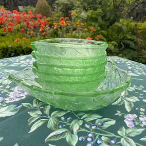 May include: A set of five green glass bowls with a leaf pattern. The bowls are stacked on top of each other and are sitting on a green tablecloth with a floral pattern.