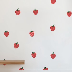 May include: A white wall with a repeating pattern of red strawberries. A wooden shelf is placed on the wall, and a brown woven rug is on the floor.