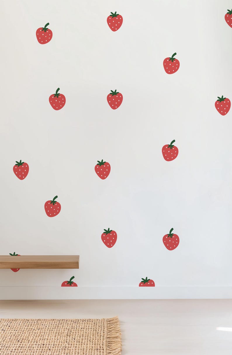 May include: A white wall with a repeating pattern of red strawberries. A wooden shelf is placed on the wall, and a brown woven rug is on the floor.