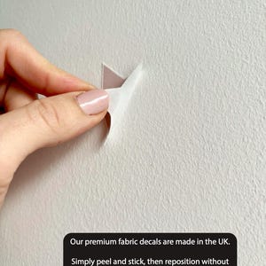 May include: A close-up of a white wall with a fabric decal being peeled away. The text on the image reads: "Our premium fabric decals are made in the UK. Simply peel and stick, then reposition without leaving any marks or damage!"