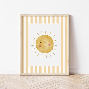 May include: A framed print featuring a yellow sun with a smiling face on a white background with yellow and white stripes on the border.