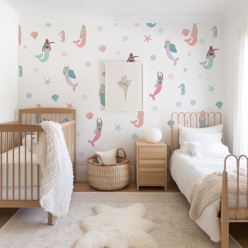 May include: A nursery with a mermaid theme. The white walls are decorated with pink, teal, and blue mermaid decals, starfish, and dots. The room features a wooden crib, a bed, a woven basket, a framed picture, and a white rug.