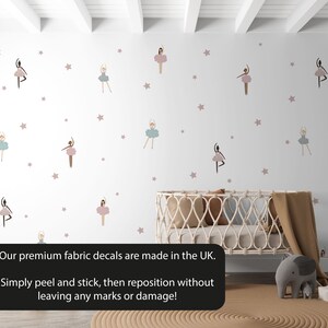 May include: A white wall with a crib and a rug. The wall is decorated with pink and blue ballerina fabric decals and pink stars. The text "Our premium fabric decals are made in the UK. Simply peel and stick, then reposition without leaving any marks or damage!" is at the bottom of the image.