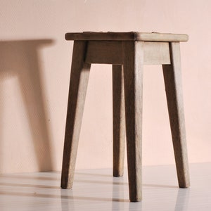 May include: A simple wooden stool with four legs. The stool is made of light brown wood and has a natural finish.
