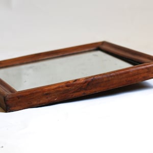 May include: A wooden framed mirror with a simple design. The mirror is slightly tilted and the frame is a dark brown color.