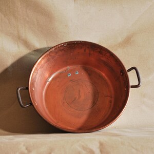 Peut inclure: Une marmite de cuisine en cuivre vintage avec deux petites poignées. Le pot est rond et brun rougeâtre, montrant des signes d'usure. Il est probablement utilisé pour cuisiner ou servir des aliments. Diamètre d'environ 25 cm.