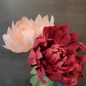 May include: Two paper flowers in a vase. One flower is pink and the other is red.