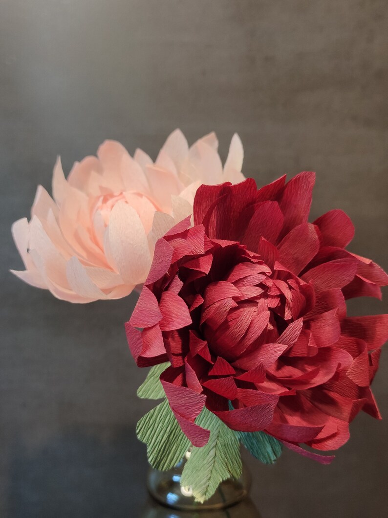 May include: Two paper flowers in a vase. One flower is pink and the other is red.