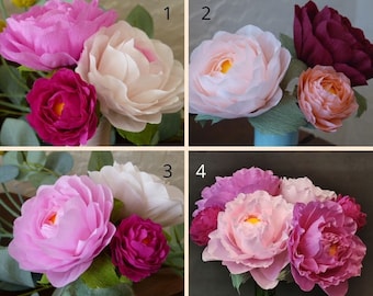Op de afbeelding: Vier verschillende arrangementen van papieren bloemen in verschillende tinten roze, wit en bordeauxrood. De bloemen zijn gerangschikt in een vaas en omringd door groen.