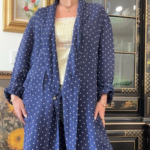 May include: A long, navy blue robe with white polka dots. The robe has long sleeves and a single button closure. The robe is open in the front, revealing a yellow top. The robe is made of a lightweight fabric.
