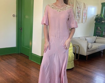 May include: A long, pink maxi dress with a lace neckline and short, ruffled sleeves. The dress is made of a lightweight fabric and has a flowy silhouette.