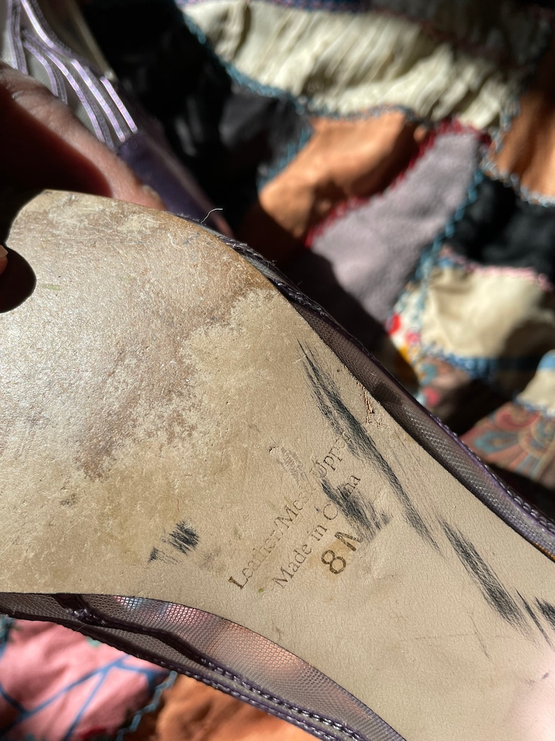 Pu&ograve; includere: Primo piano della suola di una scarpa in rete viola con il testo "Leather-Made Upper" e "Made in China" e la taglia "8 1/2".